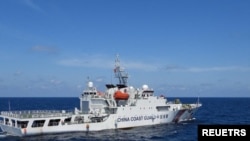 2024年2月8日,菲律賓南中國海斯卡伯勒淺灘附近,一艘中國海岸警衛隊船隻在菲律賓海岸警衛隊船隻特雷莎·馬格巴努亞號旁駛過。(路透社)
