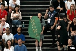 在2024巴黎奧運羽球男雙準決賽賽場上，一名女子手持台灣地圖形狀，寫有「台灣加油」字樣的標語，她的身後站著一名賽場警衛。（2024年8月4日）