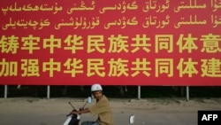 一名騎電摩托車的男子經過新疆喀什莎車縣的一面政府豎立的宣傳牌。 (2023年7月17日)