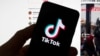 在一台顯示TikTok主螢幕的電腦前，人們看到手機上的TikTok標誌。