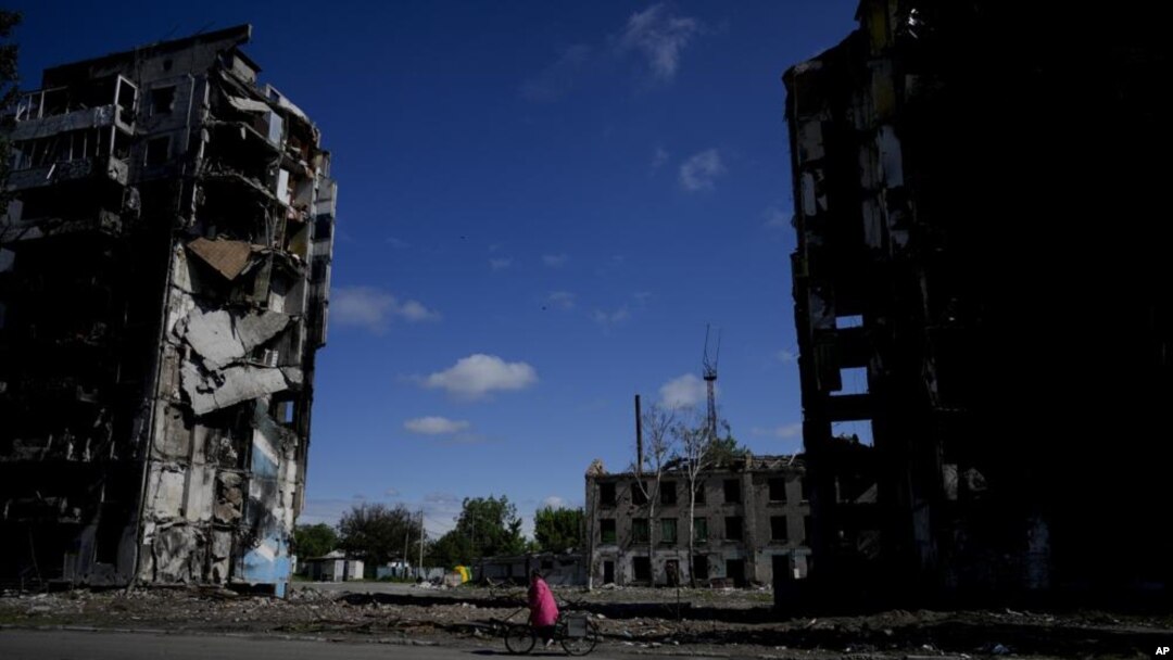 Una mujer monta en bicicleta cerca de edificios destruidos por ataques en Borodyanka, a las afueras de Kiev, Ucrania, el martes 31 de mayo de 2022. (AP Foto/Natacha Pisarenko)