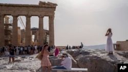 Un turista usa un abanico para enfriar a otro sentado en un banco frente al Partenón en la antigua Acrópolis, en Atenas, el 12 de junio de 2024.