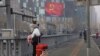 A traveler stands on a bridge near a display showing government propaganda in the fight against the COVID-19 viral illness in Beijing, China, Feb. 13, 2020.