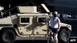 Un hombre en bicicleta pasa frente a un vehículo blindado de la Guardia Nacional cerca de la Casa Blanca, el lunes 1 de junio de 2020, cuando manifestantes se reúnen para protestar la muerte del afroestadounidense George Floyd en custodia policial.