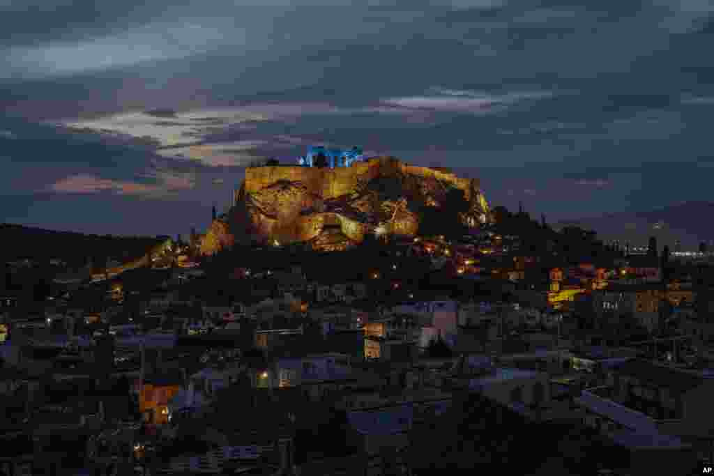 The ancient Parthenon temple atop the Acropolis hill is lit blue in Athens, Greece.