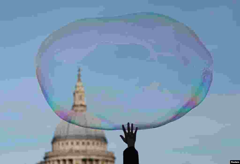 A child bursts a soap bubble as it floats past St Paul's Cathedral in London, Britain.