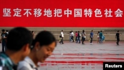 人們走過北京天安門廣場豎立的一幅宣傳中國特色社會主義道路的巨幅標語。 （2012年6月3日）