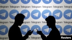 兩名使用手機的男子站在俄羅斯加密通信平台Telegram的標誌前。 （2015年11月18日）