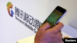在北京舉行的全球移動互聯網會議上一名參觀者在騰訊展台前玩智能手機上的遊戲。 （2015年4月28日）