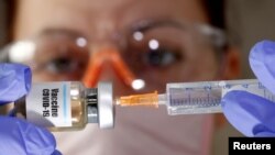 FILE - A woman holds a small bottle labeled with a 'Vaccine COVID-19' sticker and a medical syringe in this illustration taken April 10, 2020.