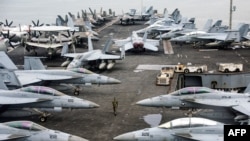 一名美國海軍軍官在馬來西亞吉隆坡郊區巴生港走過停在尼米茲級航空母艦亞伯拉罕號飛行甲板上的戰鬥機。這類核動力航空母艦的生產鏈需要重要礦物。 （2024年11月26日，）