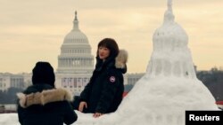 中國遊客與美國國會大廈雪雕合影，背景是真實的國會大廈，上面裝飾著美國當選總統特朗普即將就職的旗幟。 (2025年1月13日)